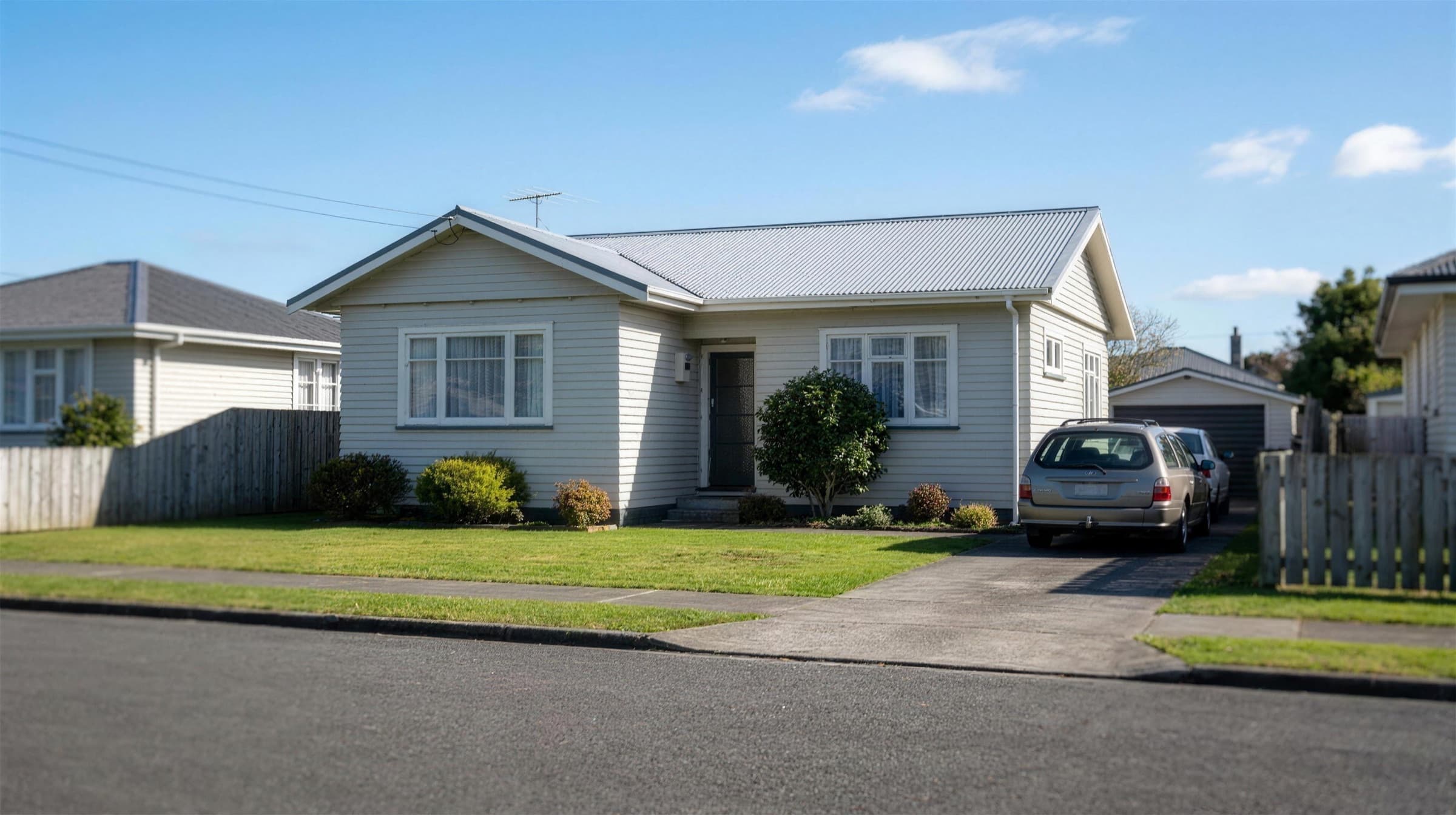 A single-storey Auckland weatherboard home with a large, clear metal roof in full sun and no shading from trees or neighbouring buildings.