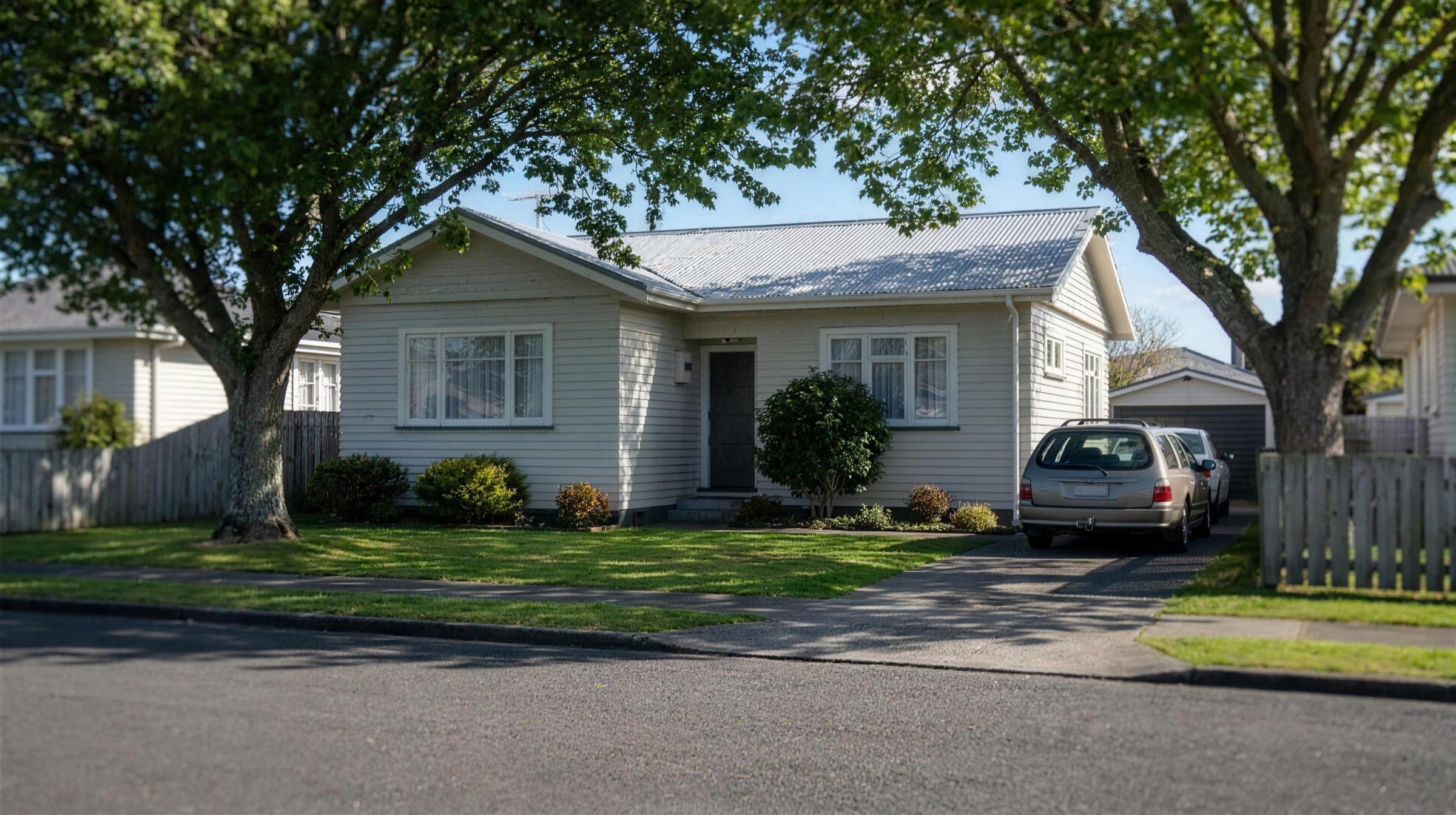 A similar Auckland weatherboard home with its roof heavily shaded by two large street trees, leaving little of the roof in direct sun.